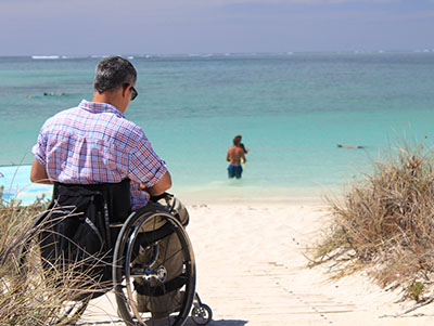 Man in rolstoel op een zomers strand, zee op de achtergrond