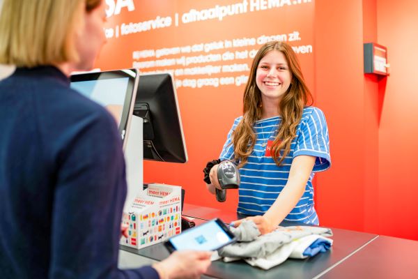 Lachende jonge medewerkster van de Hema achter de kassa