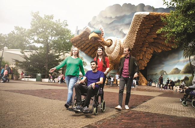 Foto van 4 personen voor de VogelRok in de Efteling, een persoon zit in een rolstoel