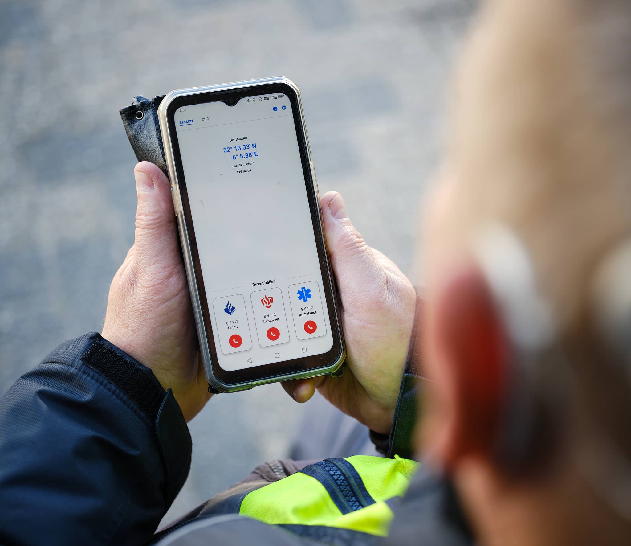 Beeld van een persoon die een mobiele telefoon in de hand heeft. Op het scherm zijn icoontjes van de brandweer, politie en ambulance zichtbaar.