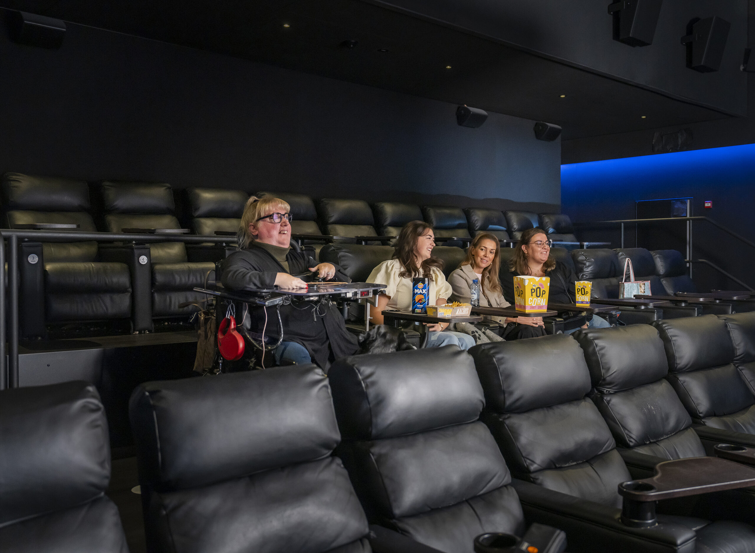 Marieke zit in haar rolstoel in de bioscoop, haar vriendinnen zitten in de stoelen naast haar.