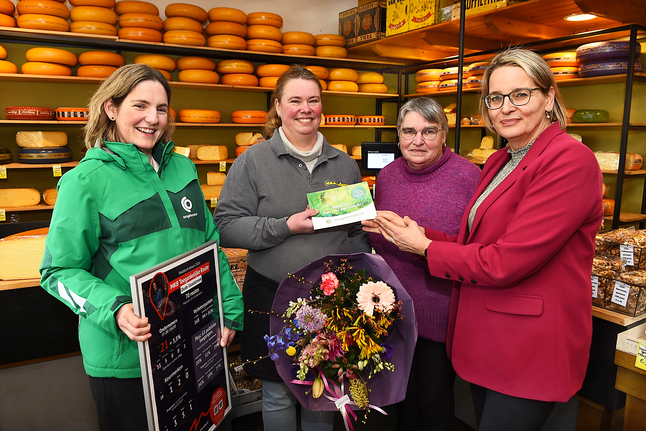 Vier dames kijken in de camera, twee van hen ontvangen het keurmerk voor toegankelijkheid